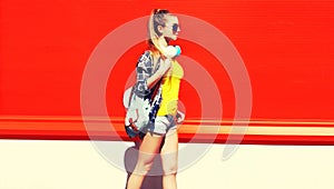 Portrait of young woman with headphones listening to music posing wearing backpack in the city on red background