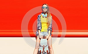 Portrait of young woman with headphones listening to music posing wearing backpack in the city on red background