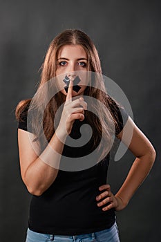 Portrait of a young woman with her mouth sealed with black tape, restriction of freedom of speech, censorship and a ban