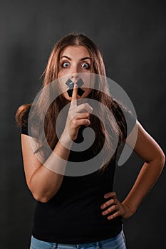 Portrait of a young woman with her mouth sealed with black tape, restriction of freedom of speech, censorship and a ban