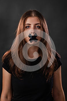 Portrait of a young woman with her mouth sealed with black tape, restriction of freedom of speech, censorship and a ban