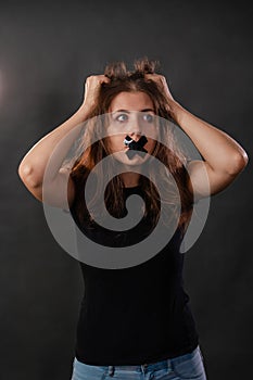 Portrait of a young woman with her mouth sealed with black tape, restriction of freedom of speech, censorship and a ban