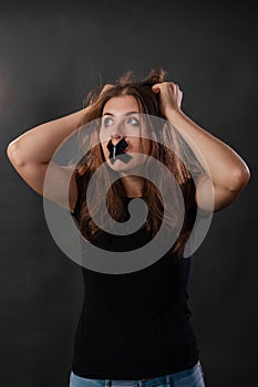 Portrait of a young woman with her mouth sealed with black tape, restriction of freedom of speech, censorship and a ban