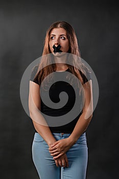 Portrait of a young woman with her mouth sealed with black tape, restriction of freedom of speech, censorship and a ban