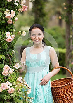 Portrait of young woman holding a basket near roses in a garden