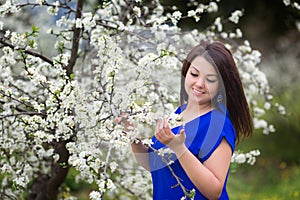 Portrait of a young woman holding a brunch of blossoming plum tree in garden, happily smiling