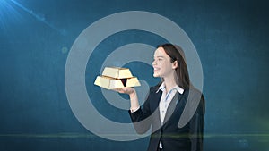 Portrait of young woman holding golden bars on the open hand palm, over isolated studio background. Business concept.