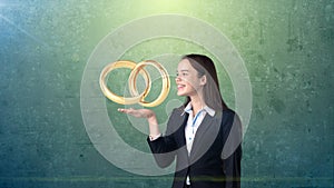 Portrait of young woman holding golden wedding rings on the open hand palm, isolated studio background. Business concept