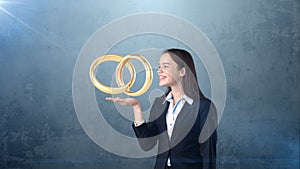 Portrait of young woman holding golden wedding rings on the open hand palm, isolated studio background. Business concept