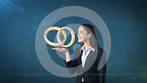 Portrait of young woman holding golden wedding rings on the open hand palm, isolated studio background. Business concept