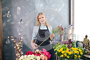 Young woman holding long flower and cutting it at florist shop