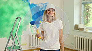 Portrait of young woman holds a wall brush roller in her hand after completing a home painting project. Female decorator