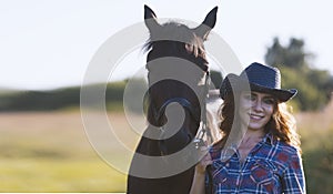 Portrait of a young woman with horse in meadow at summer day