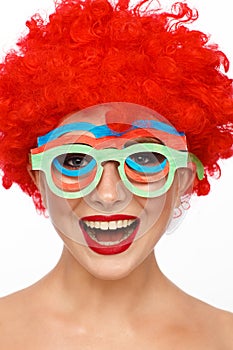 Portrait of a young woman in the image of a clown with a red wig on her head