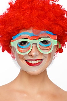 Portrait of a young woman in the image of a clown with a red wig on her head