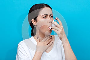 Portrait of a young woman inhaling medication during an asthma attack. Blue background. Copy space