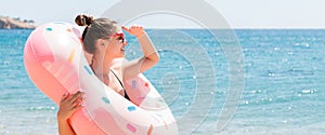 Portrait of young woman inside doughnut inflatable ring looking for somebody at the sea background. Girl is waiting for somebody