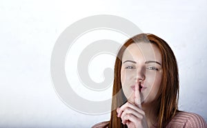 Portrait of young woman keeping finger on her lips and asking to keep quiet, over gray background, Copyspace in left side