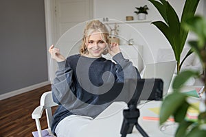 Portrait of young woman, lifestyle blogger, recording vlog video about her life and daily routine, sitting in front of