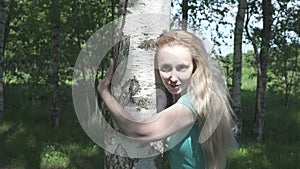 Portrait of the young woman with a long fair hair of the birch embracing a trunk in the birch wood