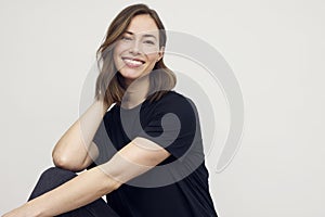 Portrait of young woman looking happy on white background. Big smile on her face, hands touching her neck.