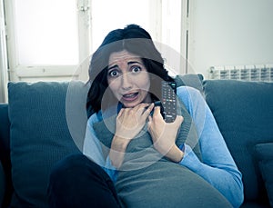 Portrait of a young woman looking scared and shocked watching scary movie on TV