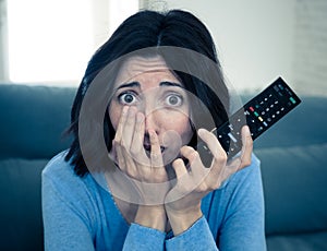 Portrait of a young woman looking scared and shocked watching scary movie on TV