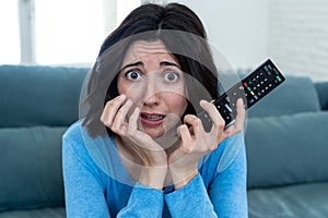 Portrait of a young woman looking scared and shocked watching scary movie on TV