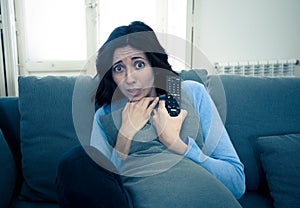 Portrait of a young woman looking scared and shocked watching scary movie on TV