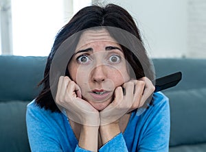 Portrait of a young woman looking scared and shocked watching TV. Human expressions and emotions