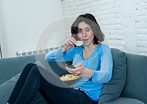 Portrait of a young woman looking scared and shocked watching TV. Human expressions and emotions