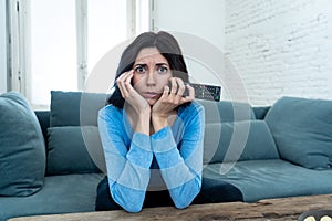 Portrait of a young woman looking scared and shocked watching TV. Human expressions and emotions