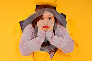 Young woman looking through a torn hole in paper wall.