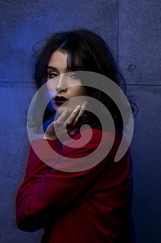 Portrait of young woman with makeup and hairstyle, wear red suit, looking at camera sensual, blue neon studio light.