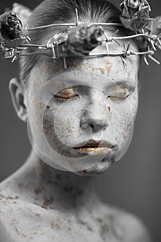 Portrait of young woman with marble skin and wearing a wreath of barbed wire and dry roses.