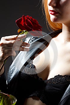 Portrait of young woman model in red dress holding red rose flower in hand over dark background in photo studio. Beauty