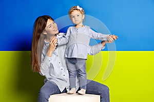 Portrait of young woman, mother with her little girl, daughter isolated over blue and yellow Ukrainian flag background