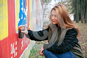 Portrait of a young woman painting graffiti with spray paint on a street wall. On open air. City concept