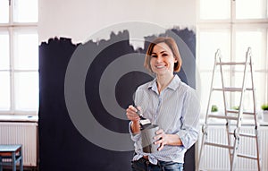 A portrait of young woman painting wall black. A startup of small business.