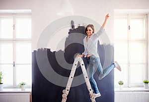 A portrait of young woman painting wall black. A startup of small business.
