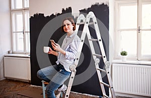 A portrait of young woman painting wall black. A startup of small business.