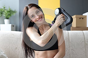 Portrait of young woman with percussion massager in her hands at home