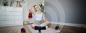 Portrait of young woman personal yoga instructor, recording workout video at home, using digital camera to vlog her