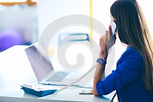 Portrait of a young woman on phone in front of a laptop computer