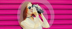 Portrait of young woman photographer taking picture on film camera on pink background