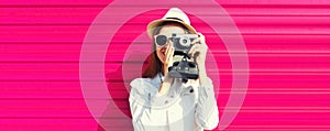 Portrait of young woman photographer taking picture on film camera on pink background