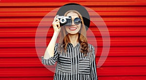 Portrait young woman photographer with vintage film camera over red wall