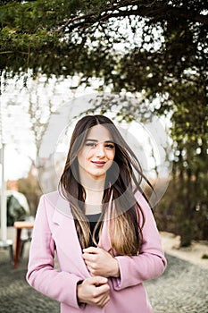 Portrait of young woman in pink cout smile on camera on city street