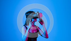 Portrait of young woman playing in VR-glasses in neon light on blue background. Concept modern gadgets and technologies