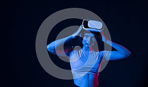 Portrait of young woman playing in VR-glasses in neon light on blue background. Concept modern gadgets and technologies
